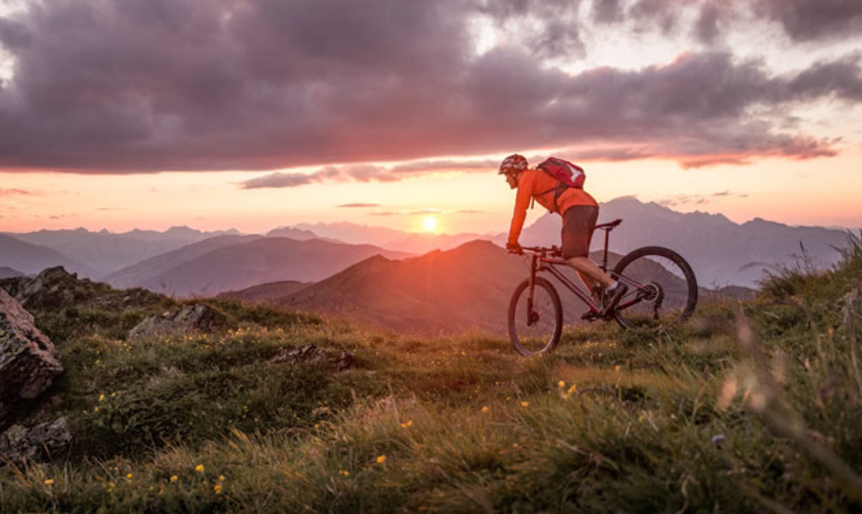 Ein Mountainbiker fährt im Sonnenuntergang am Berg.